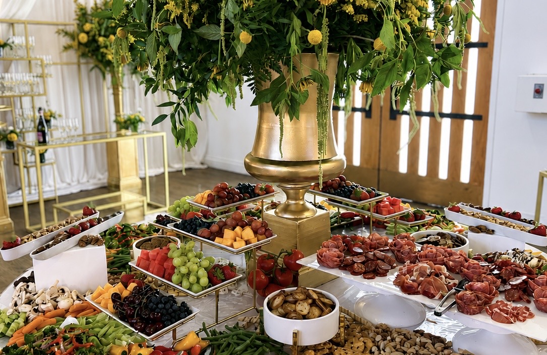 Full grazing spread with charcuterie, cheeses, fruits, breads and a tall floral centerpiece